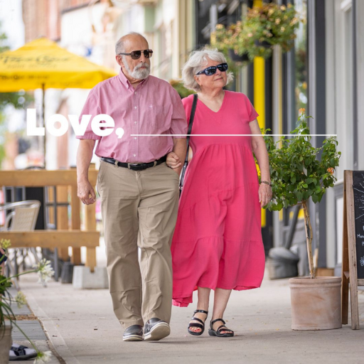 Man and woman walking down a street with shops.